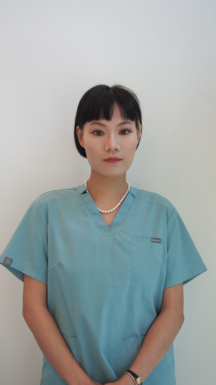 Woman with short black hair wearing teal medical scrubs and a pearl necklace.
